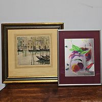 Both framed artworks side by side on a wooden surface against a plain wall