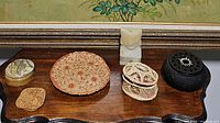 Photo displaying six assorted decorative items on a wooden surface: small carved statue, woven basket, ceramic plate, black cast iron round item, and two coasters made of resin and cork.