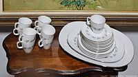 Set including tea cups stacked and arranged on table with plates and trays