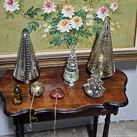 Four mercury glass Christmas trees and four accompanying ornaments displayed on wooden table.