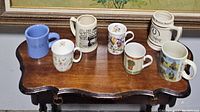 All seven coffee mugs displayed on wooden table showing a variety of designs and form factors.