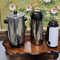 Commercial coffee maker, airpot, and thermal carafe on a wooden table in front of floral artwork