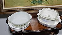 Shows the Fire King Anchor Hocking round casserole dish with green floral pattern and stack of Corningware blue cornflower pattern dishes.