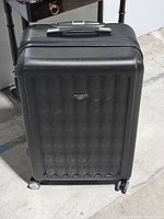 Front view of black Samsonite hard shell suitcase with wheels on the ground