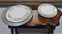 Image showing stacked plates including 3 plates with pastel colored floral wreath pattern and 1 oval metal tray underneath