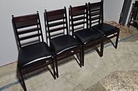 Set of four wooden folding chairs in a row on concrete floor, black vinyl seats visible, dark wood frames with a ladder back design.