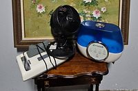 Photo showing all three items: white portable massager, black Honeywell fan, and blue PureGuardian humidifier on wooden table.