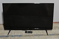 Front view of TCL flatscreen TV on feet with remote control placed in front.