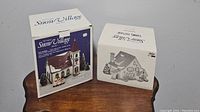 Two pieces of The Original Snow Village in their original boxes on a table, indicating lot contents and packaging condition.