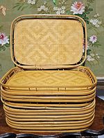 Stack of fourteen rectangular bamboo woven rattan tiki trays showing the sides and tops of trays in natural bamboo color.