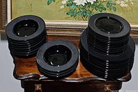 Three stacks of vintage black china on a wooden furniture surface: soup bowls on left, salad plates in middle, dinner plates on right.