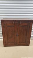 Front view of antique wooden cabinet showing two panel doors with wooden latches and metal clasp lock.