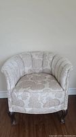 Front view of barrel chair with beige floral upholstery and wooden legs
