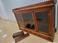 Wooden cabinet with three glass doors and three lower drawers. Parts of the cabinet's detached trim placed in the foreground.