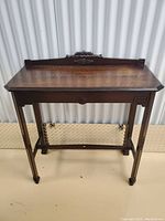 Front view of vintage walnut console table showing decorative carved back rail and single drawer.