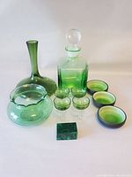 Photo showing entire collection: tall green glass vase with wide base, round scalloped green bowl, square green to clear decanter with stopper, four matching stemmed glasses, three green dipping bowls, and a green malachite trinket box.