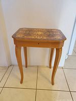 Side view of vintage Italian side table showing floral inlay on legs and tabletop, with slight wear on wood edges.