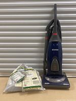 Full view of Kenmore Hepa upright vacuum with attached hose and accessories bag including replacement bags, filter, and belt.