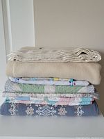 Stack of folded blankets and quilts showing variety in pattern and colors.