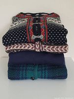 Folded stack of three sweaters; top views of patterns and solids