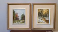 Pair of two framed oil on canvas forest scene paintings on a neutral background, showing overall condition and framing.