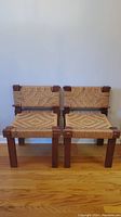 Pair of two teak frame occasional chairs side by side against a wall, front view