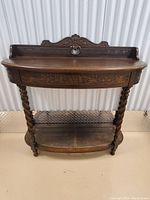 Full front view showing carved backboard with pierced cane detailing, bevelled top, carved apron, and barley twist legs supporting cane-textured shelf.