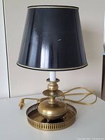 Photo showing vintage brass desk lamp with black lampshade on white background, cord visible