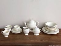 Full dish set arranged on table including teapot, creamer, sugar container, tea cups with saucers, dinner plates, side plates, and bowls.
