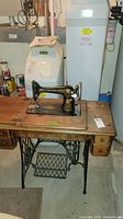 Front view of antique Singer sewing machine on cast iron base wooden cabinet with drawers in basement setting.
