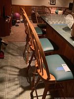 Four wooden swivel bar stools with green vinyl cushioned seats lined up at a wooden bar counter.