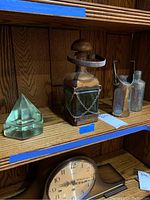 Shelf display showing all items: the ship deck prism pyramid, Italian lantern bottle with leather and brass components, and two clear glass bottles each with metal holders.
