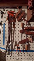Photo of multiple clamps hanging on pegboard, including wood hand screw clamps and metal bar clamps with wooden handles.