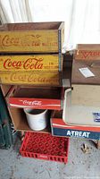 Overall display of stacked Coca-Cola wooden beverage crates with visible wear, white ceramic crock underneath, and a small red plastic crate at bottom