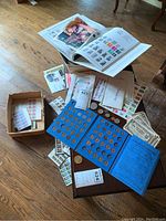 Overview of the collection showing Lincoln penny folders, coins, stamps album, and various papers on hardwood floor.
