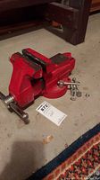 Full view of red Craftsman bench vise with serial tags and bolts placed next to it on floor.