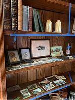 Wooden shelves with collection of books, framed and unframed pictures, postcards, and small collectibles related to Emmaus, PA local history.