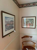 Two framed prints hung on corner walls above a wooden chair showing their general placement and framing.