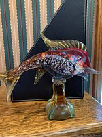 Full view of the colored glass fish sculpture showing profile and stand.