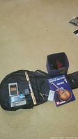 Overview of the lot showing the soft guitar case, drum sticks, guitar method book, cord, and strap on a floor.