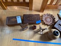 Overview of six hand carved wooden items including two boxes, a deer figurine, a small vase, a trivet, and a bowl showing carvings and wood grain