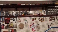Wide shot of wall-mounted pegboard with jars, tools, tape, and hardware organizers