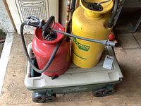 Photo of the beige-topped green plastic Ames Lawn Buddy cart with two metal pump sprayers placed inside, one red and one yellow design, shot from above showing the sprayers in the cart.