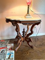 Front angle view of the ornate wood side table with white marble top, showing the scalloped marble edge and carved wood base with turned central spindle.