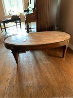 Photo of oval marble top coffee table from an angle showing wood floor and nearby furniture.