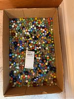 Wide view of large cardboard box full of assorted glass marbles in various colors and sizes.