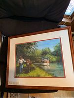 Framed watercolor painting depicting a man walking a horse near water with a boat in the background under a bright sky, framed with cream and rust double matting and brown wooden frame.