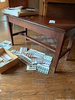 Side view of wooden piano bench showing rectangular shape, four legs, and polished surface with visible scratches.