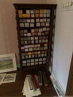 Wide view of wooden rack filled with vintage piano rolls in colored boxes, and additional rolls and papers on floor nearby.