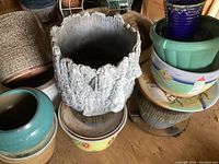Stack of various ceramic and pottery planters and pots, including the large bark-like textured planter on top of other pots with soil and chips visible